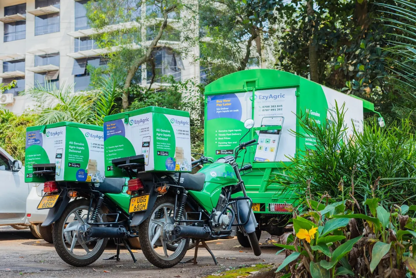 Two EzyAgric delivery motorbikes with branded delivery boxes and a green EzyAgric delivery van, parked and ready to go
