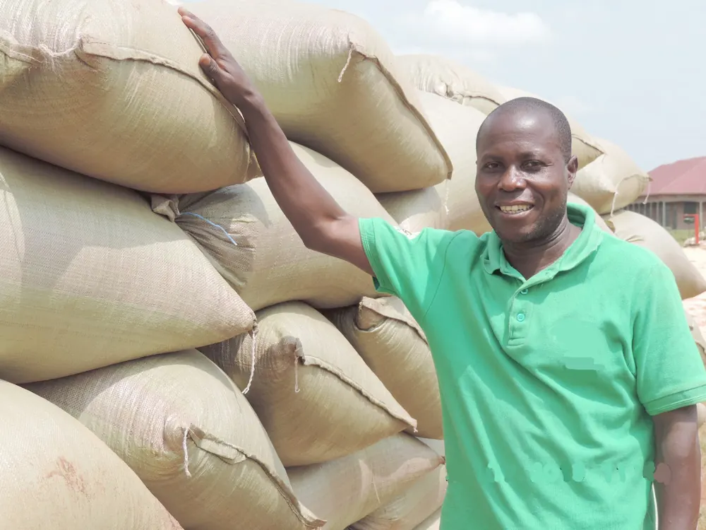 A smiling farmer beside a tall stack of produce sacks ready for market
