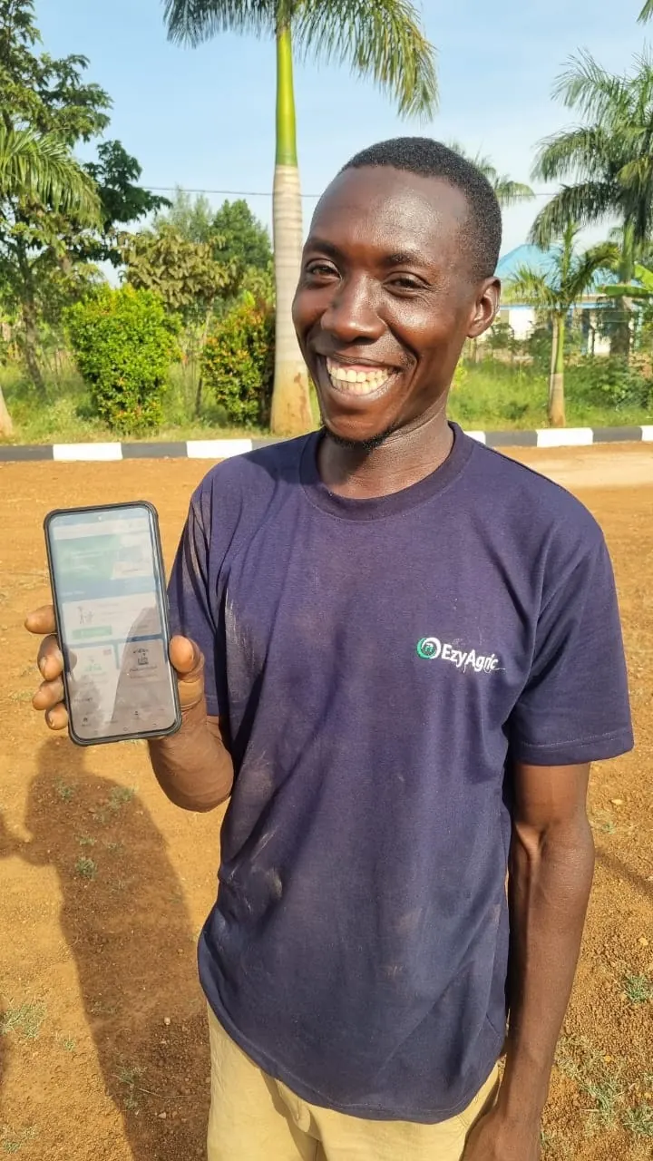A young Ugandan farmer smiling and holding his phone with the EzyAgric App