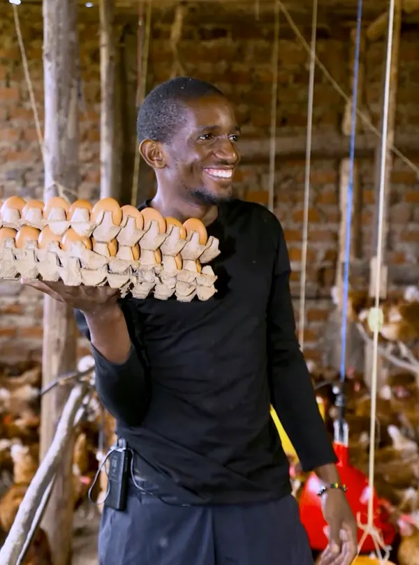 Marvin Busulwa smiles as he holds up a full tray of eggs in his poultry house